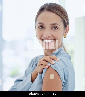 Portrait of woman with a plaster on her arm from vaccine or an injection. Young, smiling woman with patch near her shoulder from getting vaccinated Stock Photo