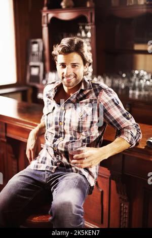 This is how I like to relax. Attractive young guy perched at a bar counter with a drink in hand. Stock Photo