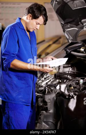 Everything seems to be in order. A male mechanic looking at some papers while working on the engine of a car. Stock Photo