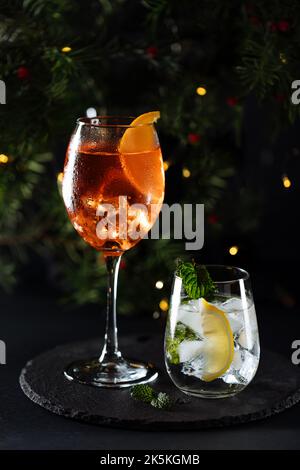 Cocktail called orange spritz and gin tonic or Moscow mule in dark party mood. Celebration scene with dark background. Christmas or New Year Party dec Stock Photo