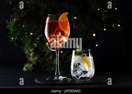 Cocktail called orange spritz and gin tonic or Moscow mule in dark party mood. Celebration scene with dark background. Christmas or New Year Party dec Stock Photo
