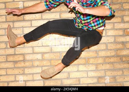That cat is fast as lightning. A cropped shot of a young man jumping with two feet through the frame in front of a brick wall. Stock Photo