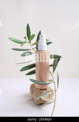 Natural cosmetic bottle of cream and an olive tree twig balancing on beige color pebble. Stock Photo