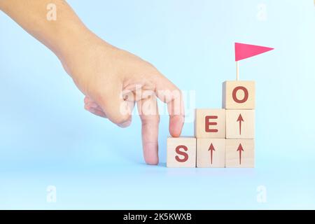 Business SEO or search engine optimization ladder to success concept. Human hand climbing wooden blocks with red flag. Stock Photo