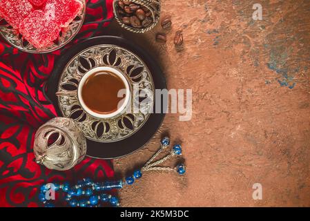 Turkish coffee cup placed with roasted coffee beans, Turkish delights and rosary beads on rustic background. Top view with copy space. Stock Photo