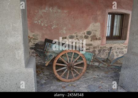 Antique wooden trailer with modern iron hook placed near ancient wall in the background and lattice on the window. Stock Photo