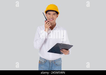 Portrait young asian man is engineer wearing helmet standing and using radio for speak with confident while holding report document isolated on white Stock Photo