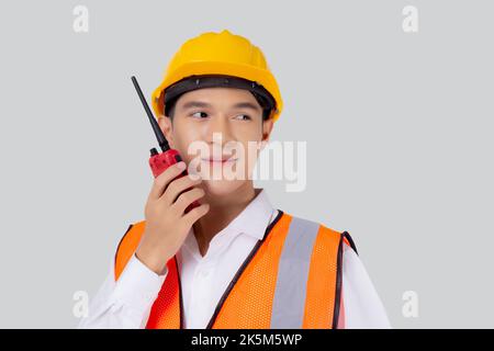 Portrait young asian man is engineer wearing helmet standing and using radio for speak with confident isolated on white background, handsome male is a Stock Photo