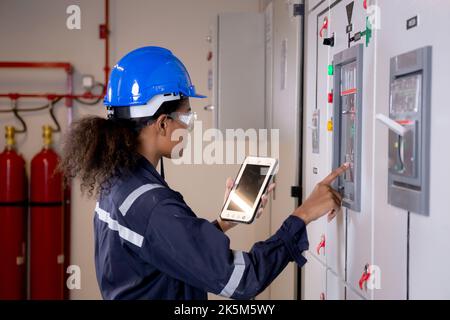Electrical young asian woman engineer examining maintenance cabinet system electric and using tablet in control room at industrial factory, technician Stock Photo