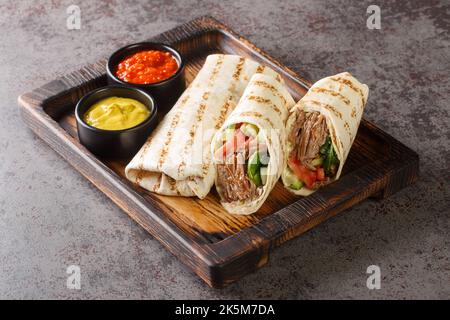 Shawarma sandwich gyro fresh roll of lavash closeup on the wooden board on the table. Horizontal Stock Photo