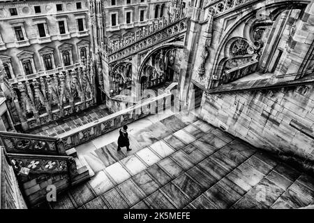 A woman walks towards one of the massive flying buttress and ornately carved stonework on the roof of the Duomo Milano (Milan Cathedral), Italy Stock Photo