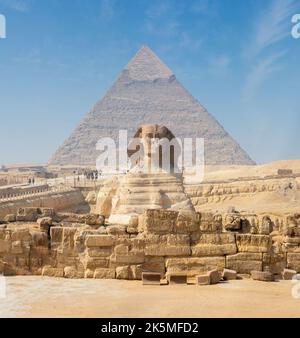 Egyptian Great Sphinx full body portrait with head, feet with all pyramids of Menkaure, Khafre, Khufu in background on a clear, blue sky day in Giza Stock Photo