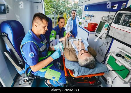 Paramedics performing electrocardiogram on mature patient lying on gurney with electrodes placed on his chest in ambulance. Cardiac patient in ambulan Stock Photo