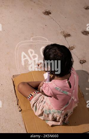 poor child studying and writing on road with chalk in absence of books Stock Photo