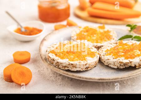 Carrot jam with puffed rice cakes on gray concrete background. Side view, close up, selective focus. Stock Photo