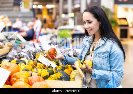 Smiling woman checks on pumpkins offered for sale in the grocery store. Stock Photo