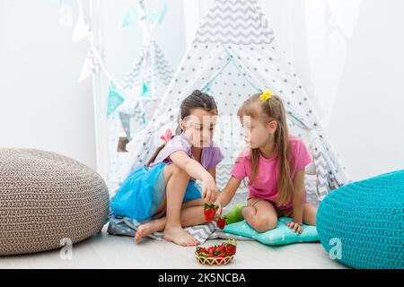 Two little cute girls sitting and eating strawberries. Stock Photo