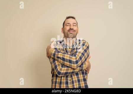 You don't need a girlfriend if you can hug yourself. Selfish feeling concept. Funny latin man in plaid shirt hugging himself and smiling with pleasure Stock Photo