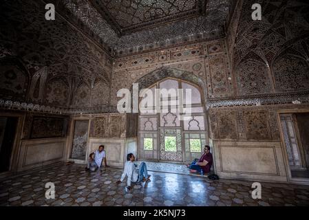Three men sitting on the floor in front of an elaborated window (jarokha), Fort Lahore, Pakistan Stock Photo