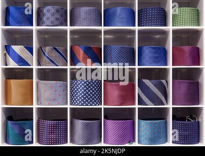 Showcase with multicolored ties. View of different colors ties in showcase. Showcase of rolled neckties at store. Coiled ties on shelf at shop. Twiste Stock Photo