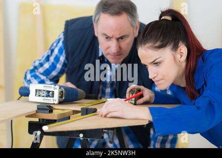 supervisor watching over female apprentice carpenter having difficulties Stock Photo