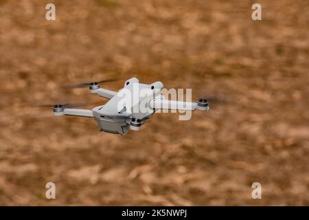 A flying camera drone or multicopter with spinning rotors isolated outdoors hovering above a field Stock Photo