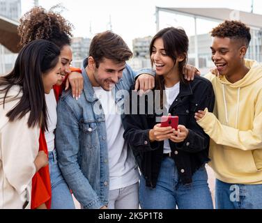 Group of young diverse smiling millennial friends looking at a mobile phone having a good time. having fun Stock Photo