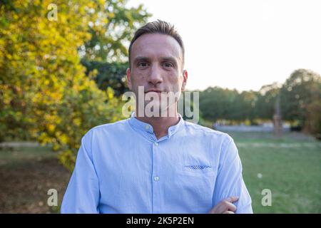 Portrait of a man in his 30s standing still in the park with crossed arms looking at the camera. Stock Photo