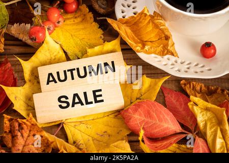 Autumn sale concept wooden block with the inscription, Colorful leaves, cup with hot coffee, viburnum fruits, Background from old boards Stock Photo