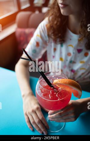 female drinking red grapefruit juicy cocktail with straw in cafe or restaurant Stock Photo