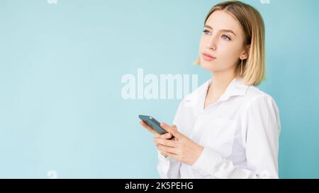 Online shopping. Office woman. Mobile technology. Advertising background. Thoughtful lady thinking about purchase smartphone in hands isolated blue co Stock Photo