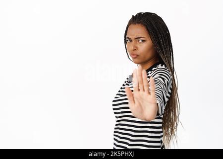 Stop this. Serious african woman extending hand at camera, showing palm taboo gesture, stopping, saying no, standing over white background Stock Photo