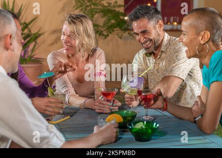 Group of multicultural cheerful friends at night party drinking cocktails and having fun together. Enjoying nightlife beverages. Stock Photo