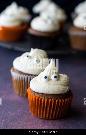 Pumpkin spice cupcakes with ghost shaped icing tops and eyeballs. Stock Photo