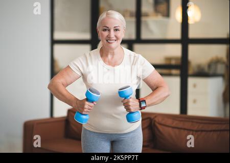Cheerful lady exercising with hand weights indoors Stock Photo