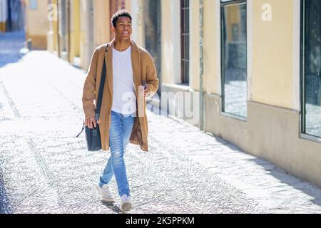 Young black man walking down the street carrying a briefcase and a smartphone. Stock Photo