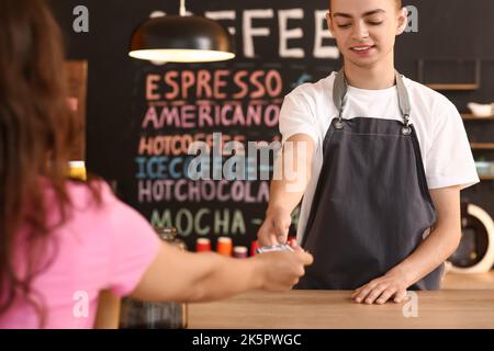 Young male barista receiving payment from visitor in cafe Stock Photo