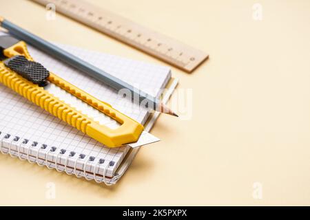 Utility knife with pencil, ruler and notebook on beige background, closeup Stock Photo