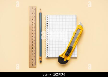 Utility knife with pencil, ruler and notebook on beige background Stock Photo