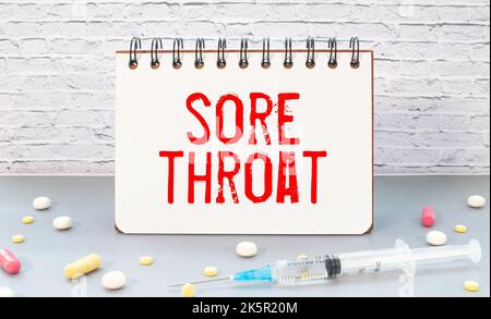 Medical concept. On a brown surface lies a stethoscope, pills and a notepad with the inscription - Sore Throat Stock Photo
