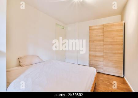 Comfortable bed with ornamental blanket placed near glass door and wardrobe in light bedroom Stock Photo