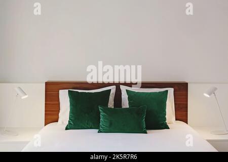 Modern bedroom in white colors with wooden headboard and green velvet accent pillows Stock Photo