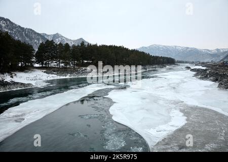 Melted ice in the bed of a beautiful river surrounded by snow-capped mountains on a winter morning before sunset. Katun river, Altai, Siberia, Russia. Stock Photo