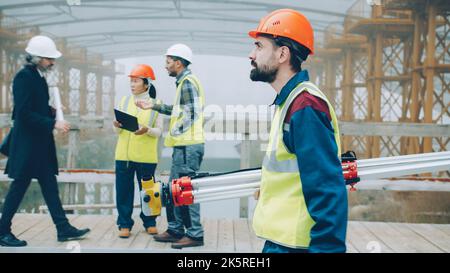 serious male surveyor in uniform walking in construction site holding theodolite concentrated on work. People and profession concept. Stock Photo