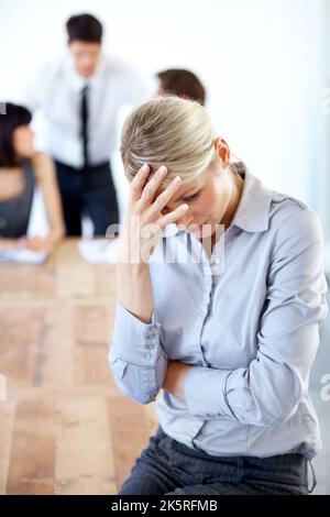 Dont let work stress you out. A stressed businesswoman holds her head in her hand looking away - blurred business colleagues in the background. Stock Photo