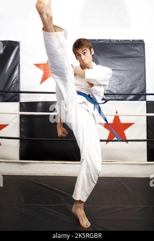 Roundhouse kick. Full length shot of a young martial artist practicing karate in the ring. Stock Photo