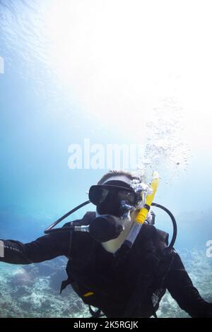 Finding recreation beneath the waves. Young woman scuba diving in the beautiful ocean with the bright sun shining through the water - Copyspace. Stock Photo