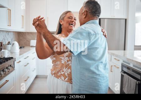 Happy senior couple, dance and laughing in joyful happiness for relationship bonding in the kitchen at home. Elderly man and woman with smile dancing Stock Photo