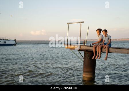 Two boys fishing with a fishing rod on a lake at sunset. Children's summer vacation Stock Photo