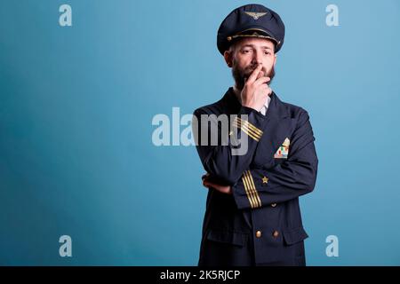 Thoughtful unsure airline pilot in uniform thinking, touching chin ...